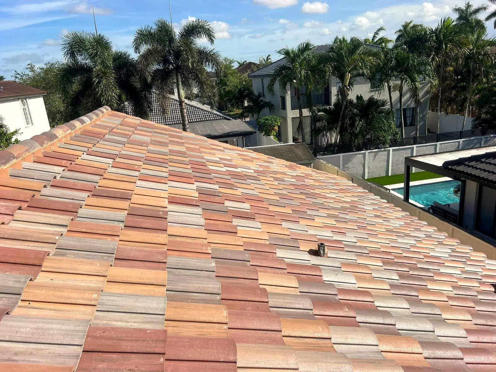 Finished blend-color tile roof beside a pool, with palm trees behind
